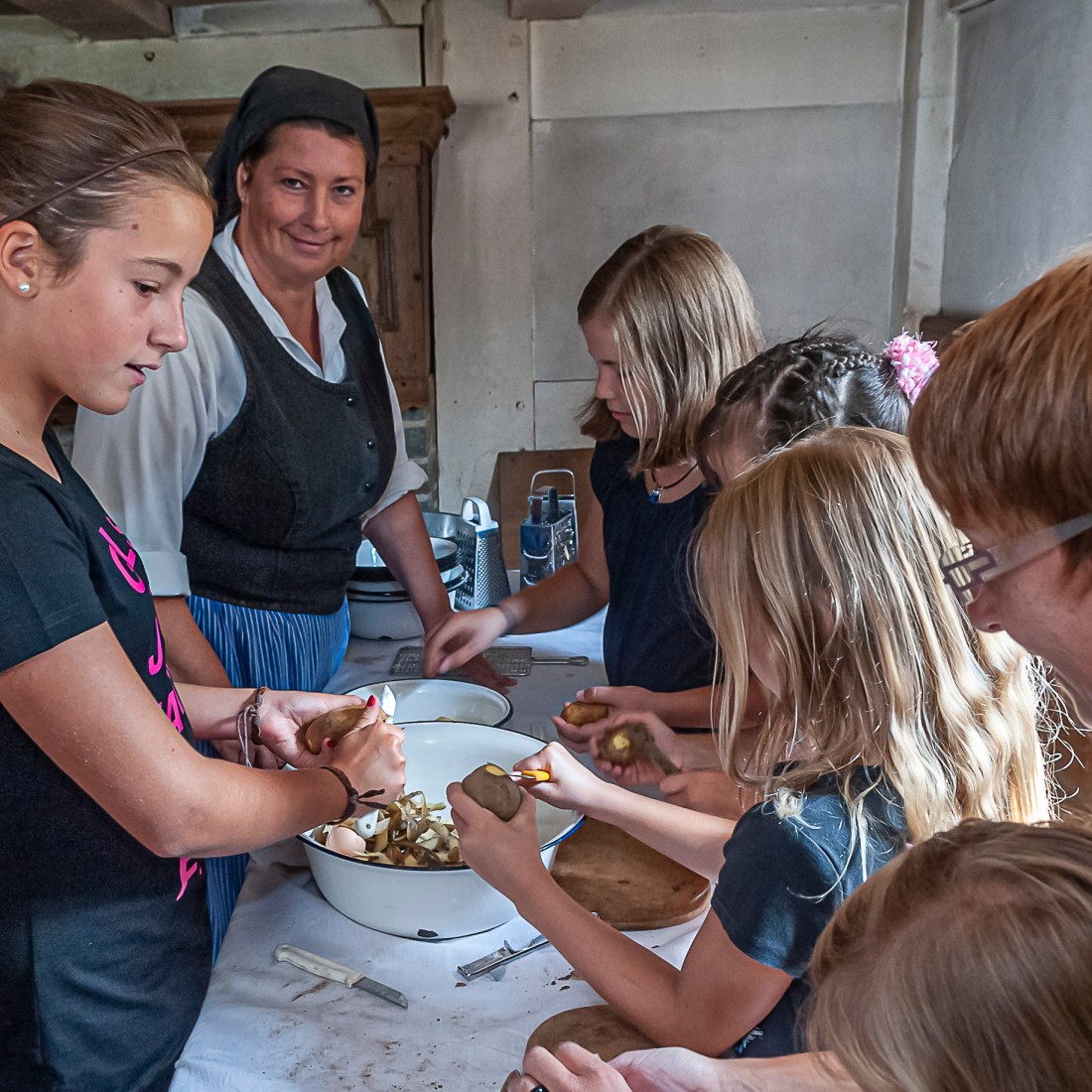 Kinder stehen an einem Tisch und schälen Kartoffeln
